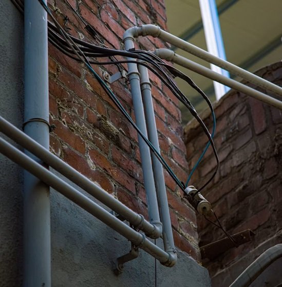 Multiservices A.D. analiza instalación de tuberías de fontanería externa en fachada de ladrillo conviviendo de forma peligrosa con cableado eléctrico desprotegido.